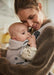 BabyBjörn Harmony baby carrier in beige with a baby held close to an adult's chest indoors.