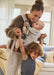 BabyBjorn Harmony baby carrier in beige with a baby being carried indoors by a smiling adult.