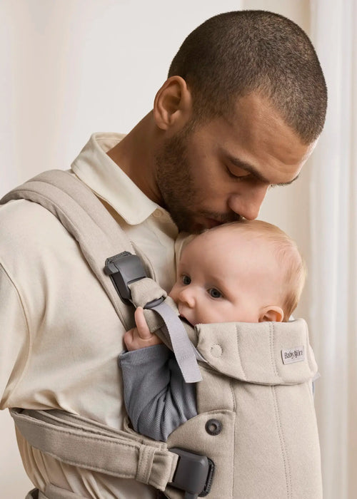 BabyBjörn Harmony baby carrier in beige with a baby held close by an adult indoors