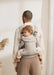 BabyBjorn Harmony baby carrier in beige holding a baby on an adult's back indoors.