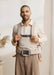 BabyBjorn Harmony baby carrier in beige worn by an adult holding a baby indoors.