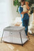 BabyBjorn Play Yard Light Silver set up in a cozy living room with a parent holding a baby nearby.