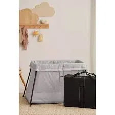 BabyBjorn Play Yard Light Silver set up in a cozy nursery with a travel bag beside it.