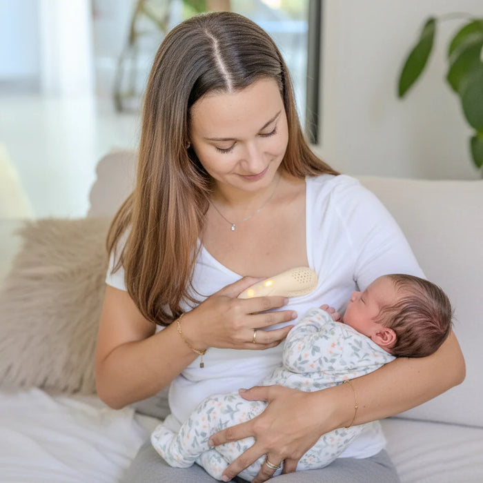 BBLüv Mumpulse 3-in-1 lactation massager used by a mother holding a newborn baby on a couch.