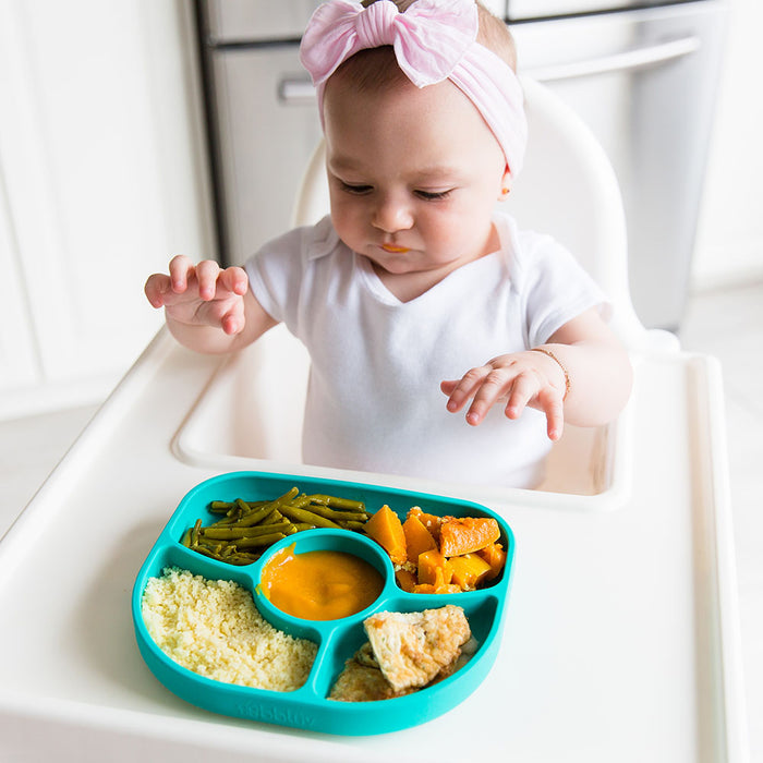 Baby in high chair with aqua silicone divided plate of vegetables and puree meal