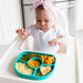 Baby in high chair with aqua silicone divided plate of vegetables and puree meal