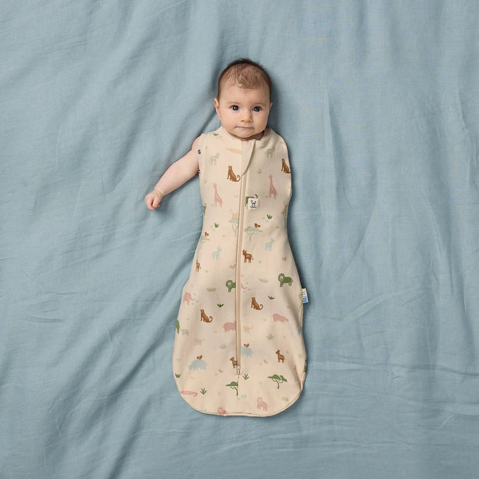 Cocoon Swaddle Sac 0.2 TOG in oatmeal with animal print, worn by baby lying on blue sheet.