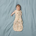 Cocoon Swaddle Sac 0.2 TOG in oatmeal with animal print, worn by baby lying on blue sheet.