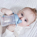 b.box silicone sippy cup in blue held by baby lying on a white quilted blanket.