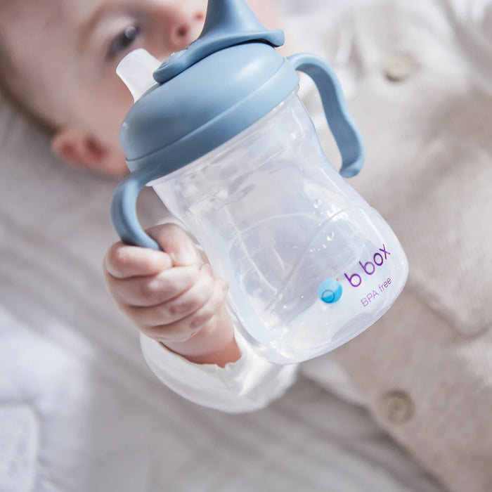 b.box silicone sippy cup in blue held by baby on a soft white blanket