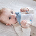 b.box silicone sippy cup in ocean color held by baby lying on a soft white blanket