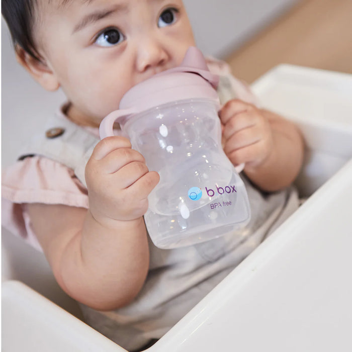 Bbox silicone sippy cup in blush color held by a baby sitting in a high chair.