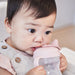 Bbox silicone sippy cup in blush held by a baby sipping from the spout.