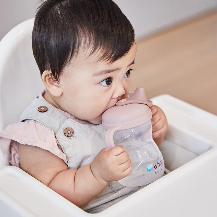 bbox training silicone sippy cup in blush held by baby sitting in high chair
