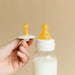 BIBS glass baby bottle with latex nipple and pacifier held by hand against beige background.