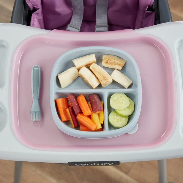 Baby divided silicone plate with banana, carrots, and cucumber on a high chair tray, next to fork.