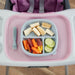 Baby divided silicone plate with banana, carrots, and cucumber on a high chair tray, next to fork.