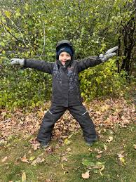 Conifere Ginko Snowsuit in charcoal, worn by a child standing with arms outstretched outdoors.