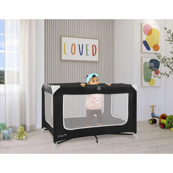 Baby standing in black portable play yard in modern nursery with toys and wall art