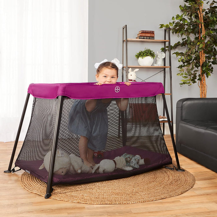 Dream On Me Travel Light Playard in pink shown with a baby standing inside in a living room.