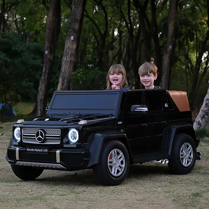 Kids electric ride-on Mercedes G63 car with two children sitting inside, shown outdoors in a park.