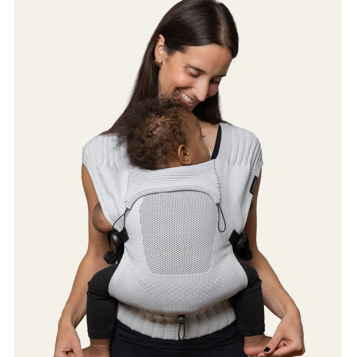 Flybaby 3D baby carrier in light grey shown worn by an adult carrying a baby on their chest.