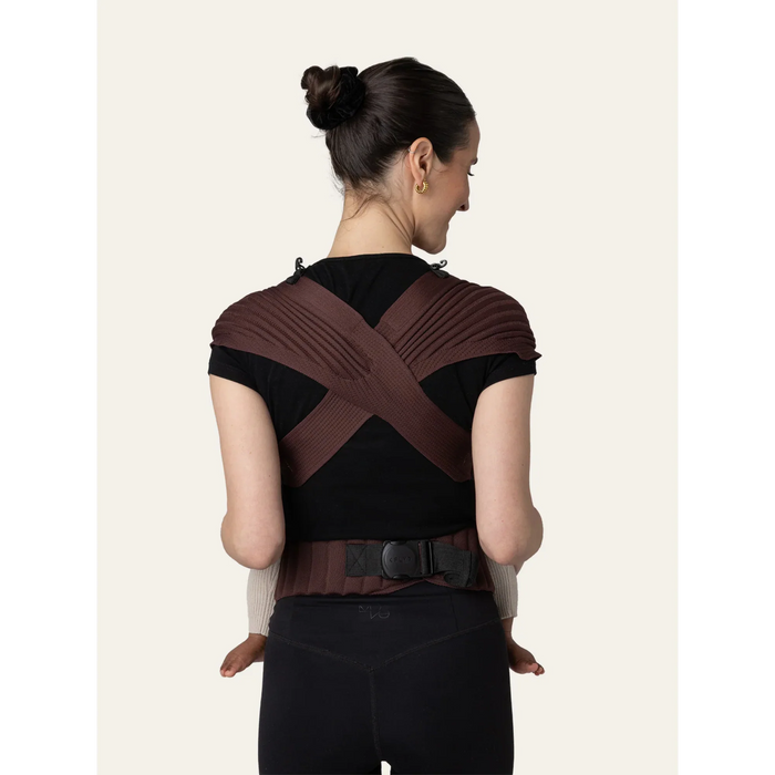 Flybaby 3D baby carrier in brown shown on a woman from the back, holding a baby.