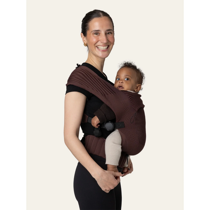 Flybaby 3D baby carrier in brown shown worn by an adult with a baby in front-carry position.
