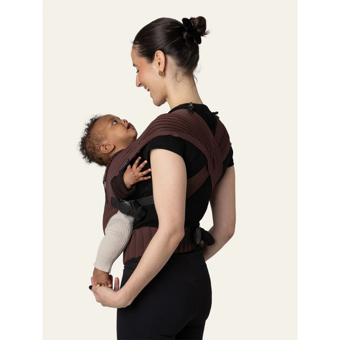 Flybaby 3D baby carrier shown on a woman with a baby facing inward, both smiling.