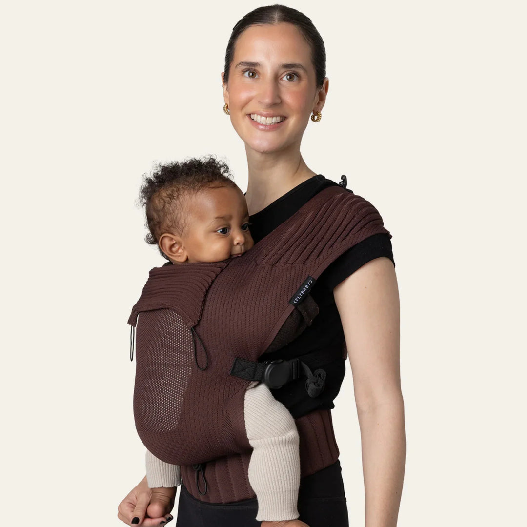 Flybaby 3D baby carrier in brown, shown worn by an adult carrying an infant on their chest.