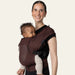Flybaby 3D baby carrier in brown, shown worn by an adult carrying an infant on their chest.