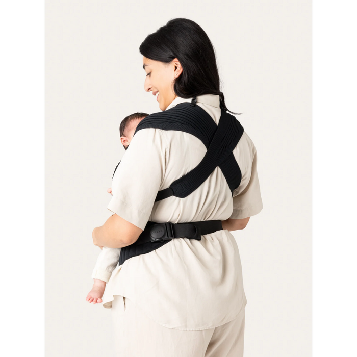 Flybaby 3D baby carrier shown on a woman carrying an infant, with black cross-strap design.