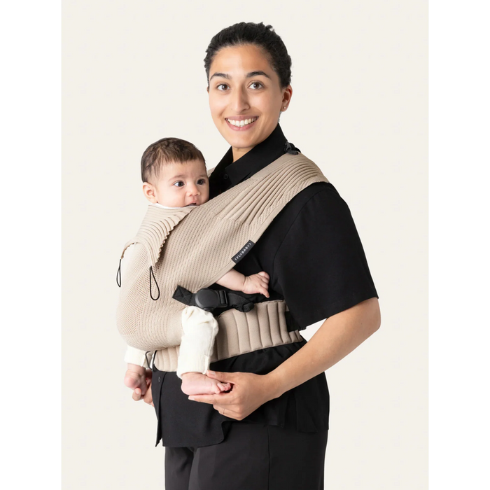 Flybaby 3D baby carrier in beige shown worn by an adult holding a baby against a neutral background.