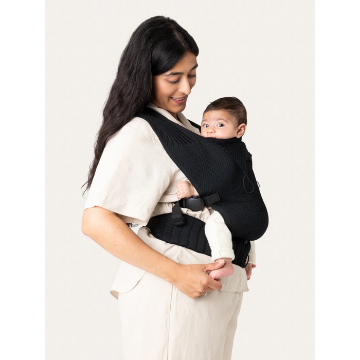 Flybaby 3D Baby Carrier in black shown on a woman carrying an infant facing inward.