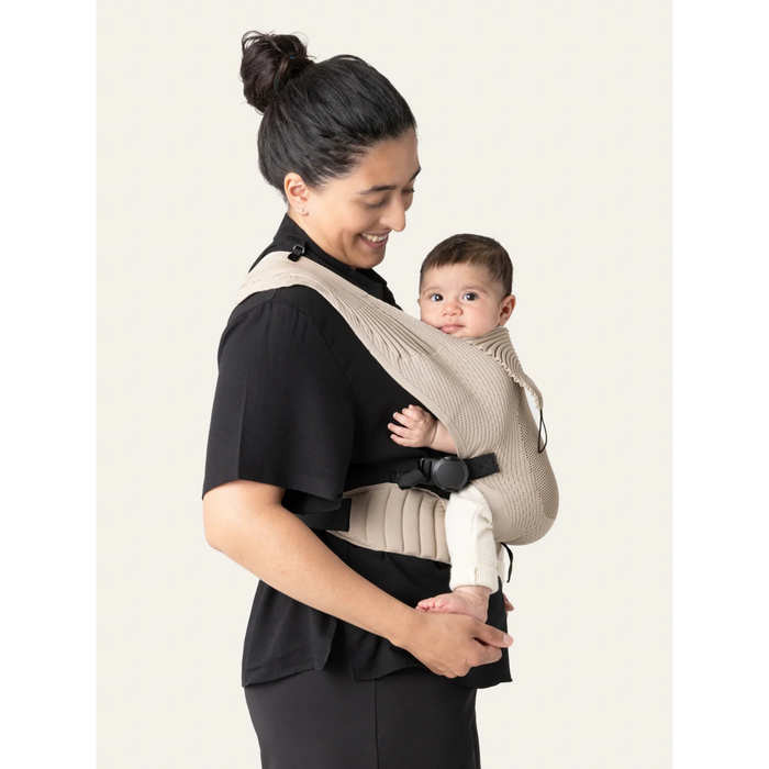 Flybaby 3D baby carrier in beige shown worn by an adult carrying a baby on their chest