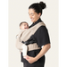 Flybaby 3D baby carrier in beige with a smiling baby carried by an adult wearing black.