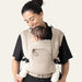 Flybaby 3D baby carrier in beige shown worn by an adult holding an infant on their chest.