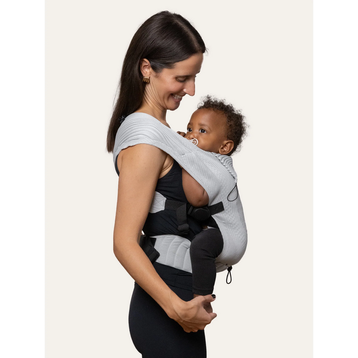 Flybaby 3D baby carrier worn by a woman carrying an infant in a front-facing position