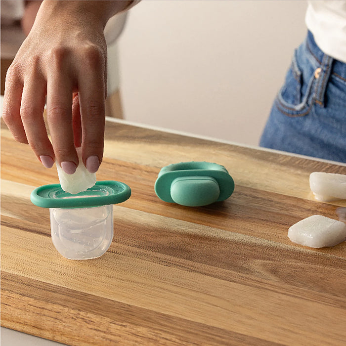Frida Baby Push Pop Feeder being filled with ice by a hand on a wooden countertop.