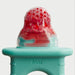 Frida Baby Push Pop Feeder with red frozen fruit inside on a plain background.