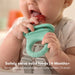 Frida Baby Push Pop Feeder held by a baby in a high chair, baby chewing on the feeder filled with fruit.