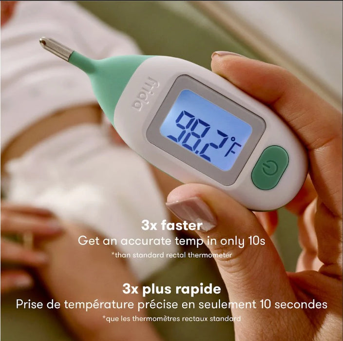 Frida Baby Quick-Read Rectal Thermometer held in hand, digital display showing 98.7°F, baby in background.