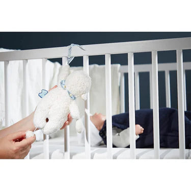 Kaloo Nomand musical sheep plush toy hanging on a crib, next to a sleeping baby.