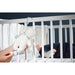 Kaloo Nomand musical sheep plush toy hanging on a crib, next to a sleeping baby.