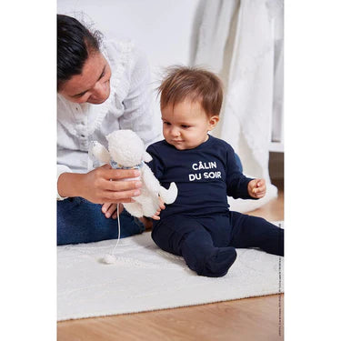 Kaloo Nomand Musical Sheep Plush Toy shown being held by an adult next to a seated baby on a rug.