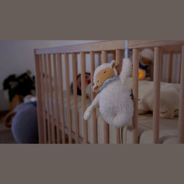 Kaloo Nomand Musical Sheep Plush Toy hanging on a crib rail in a softly lit nursery.