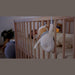 Kaloo Nomand Musical Sheep Plush Toy hanging on a crib rail in a softly lit nursery.