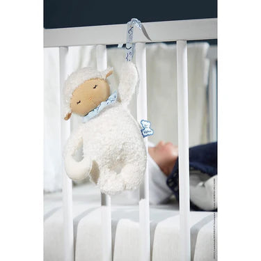 Kaloo Nomand musical sheep plush toy hanging on a white crib next to a sleeping baby.