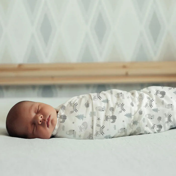 Koala Baby 4-Pack Flannel Receiving Blankets with woodland prints, wrapped around a sleeping baby on a bed.