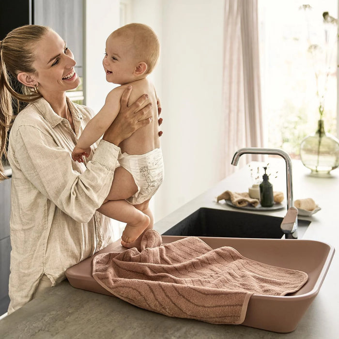 Leander Matty baby changing waterproof mat on a countertop with a smiling baby and parent nearby.